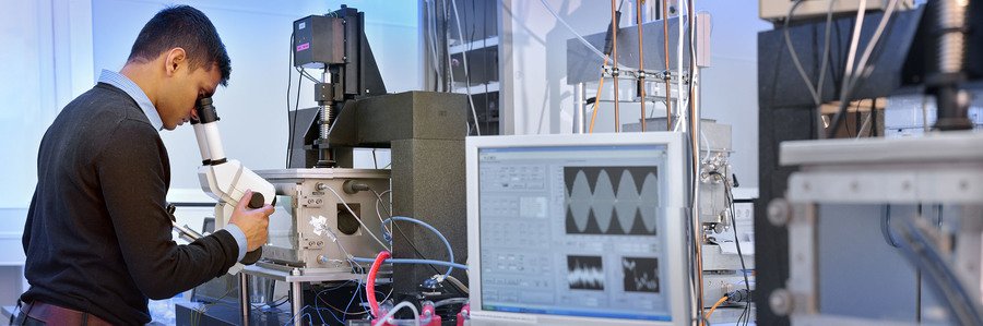 Laboratory setup with advanced equipment and computer screen displaying graphs. A scientist is looking into a microscope.