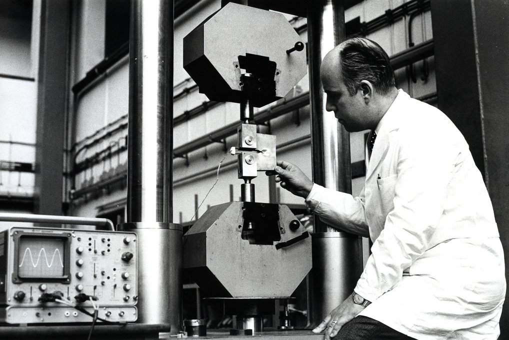 Systematische Untersuchungen zu Rissbildung und Bruch am Max-Planck-Institut für Eisen-forschung: eine zwischen zwei Spannbacken eingespannte Kompaktprobe mit vorgearbeiteter Kerbe wird Zug und Biegung ausgesetzt. Die dabei stattfindende Rissaufweitung und die Zugkraft werden elektronisch gemessen, 1975.