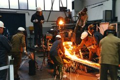Institute staff members during thin strip casting: The melt is poured from the pouring ladle into the distributor. The white-hot strip leaves the caster and runs on to the roller table for further processing, 1998.
