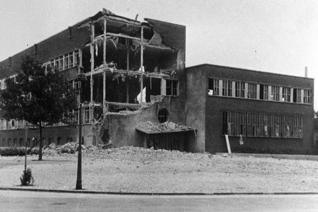 Large brick building with significant damage, showing collapsed sections and debris.