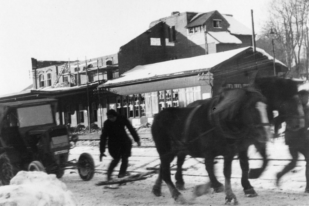 Horses and a person in front of a snow-covered building.