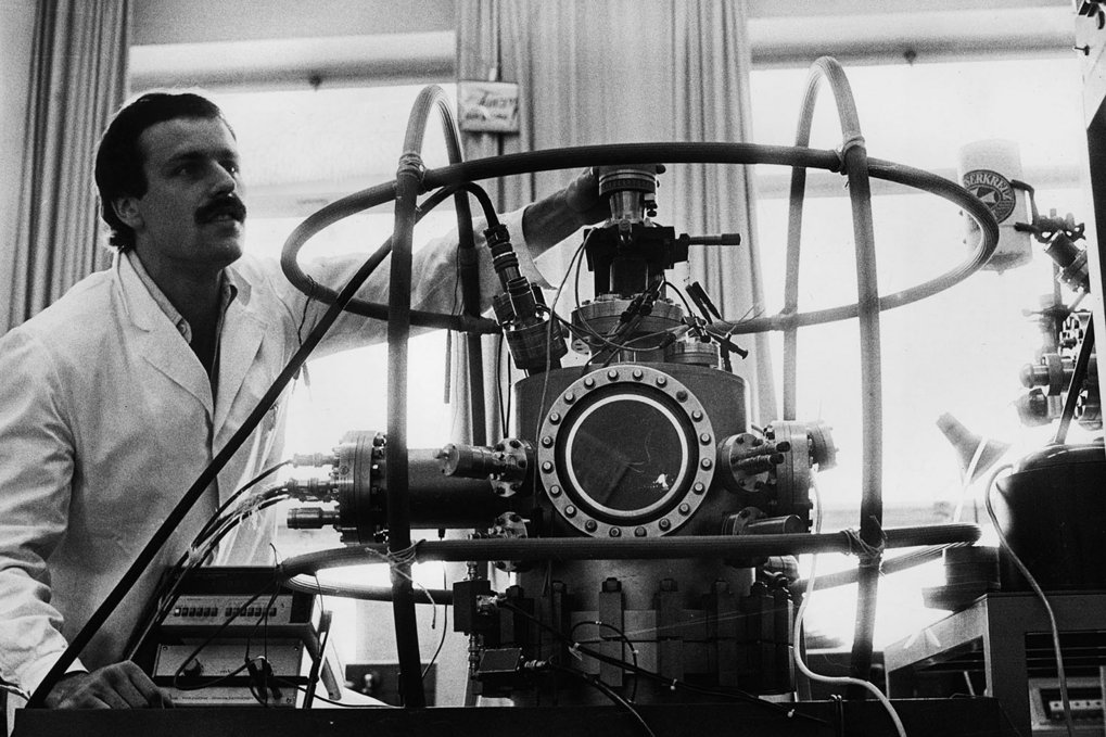Scientist with complex machinery in a lab setting.