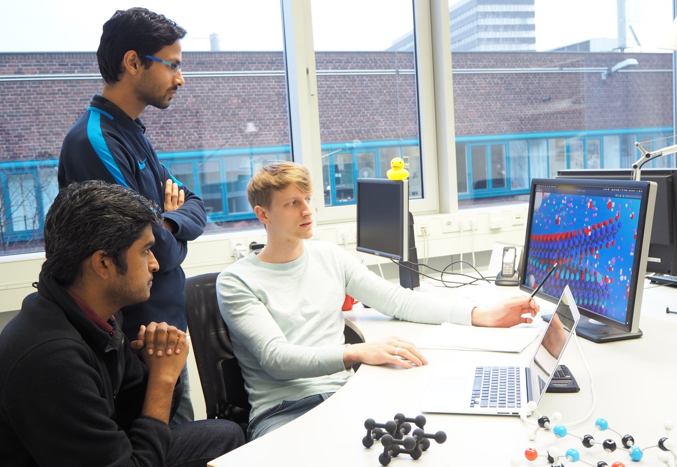 Dr. Michael Ashton (on the right) explaining his work about etching reactions for MAX compositions to his colleagues Sudarsan Surendralal (in the front left) and Ankit Gupta, doctoral students in the Computational Materials Design department.