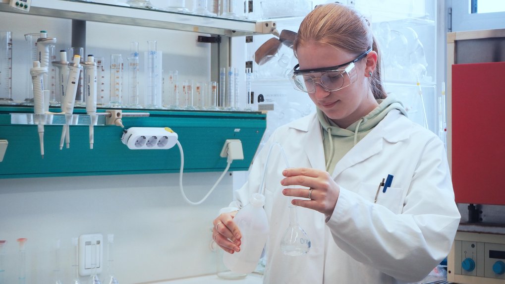 Person mit Schutzbrille und Schutzkittel in einem Chemielabor.