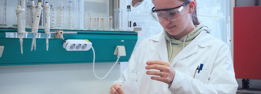 Chemielaborant*in, dual(m/w/div) Person mit Schutzbrille und Schutzkittel in einem Chemielabor.