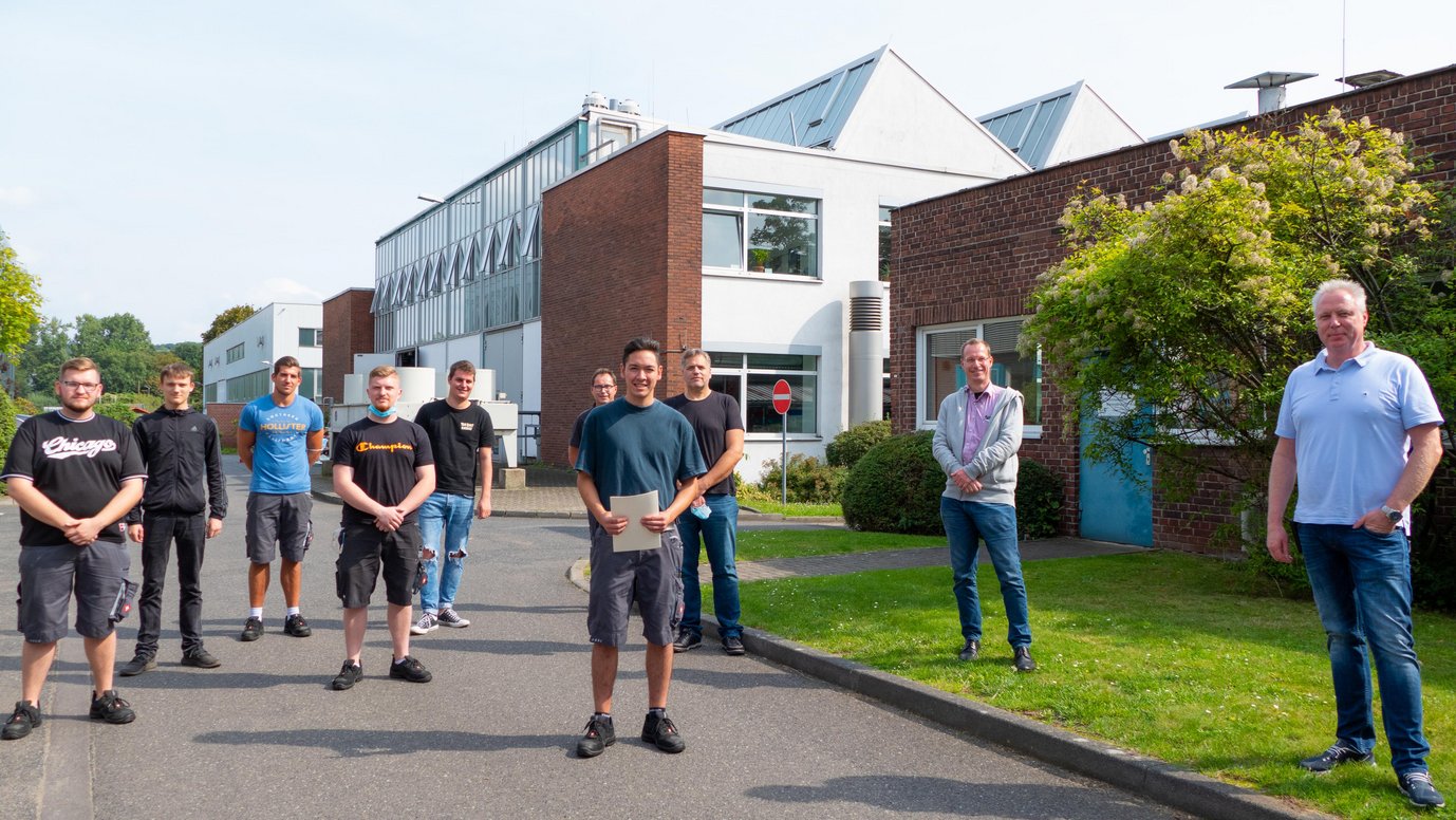 Simon Sprengel (Mitte) mit seinen Kollegen, Ausbilder Ralf Selbach (hinten rechts) und Geschäftsführer Kai de Weldige (zweiter von rechts) bei der Feier vor dem Werkstatttor am MPIE.