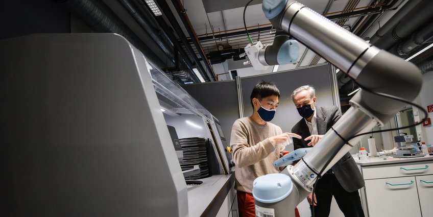 © Frank Vinken, Max-Planck-Gesellschaft In a laboratory, two individuals focus on a robotic arm, surrounded by various technical equipment and storage units.