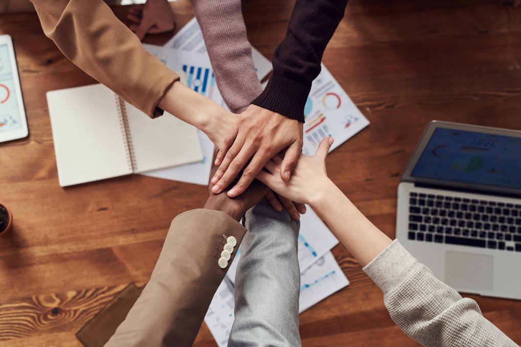 Multiple hands stacked in teamwork gesture on a wooden table.