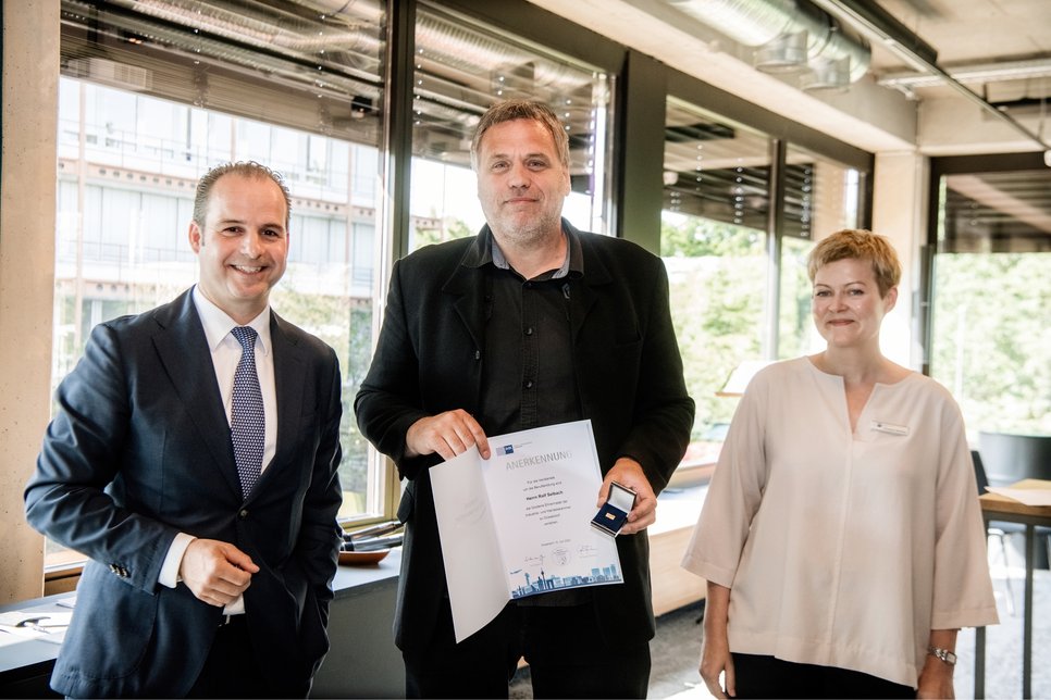 Ralf Selbach (Mitte) ist Ausbilder am MPIE und erhält die Goldene Ehrennadel der IHK Düsseldorf. Links ist der Vizepräsident der IHK Düsseldorf, Marcel Abel, zu sehen. Rechts die Leiterin des Bereichs „Ausbildung und höhere Berufsausbildung“, Christine Mertens.