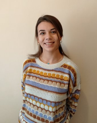 A knitted sweater displaying a pattern of horizontal stripes and circles in hues of blue, brown, yellow, and beige.