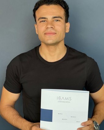 A person wearing a black T-shirt is holding a folder labeled "ICAMS," which stands for Interdisciplinary Centre for Advanced Materials Simulation, with a blue square design and text elements.