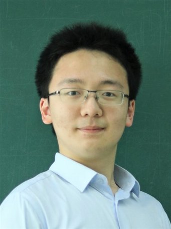 A person with dark, short hair is wearing a light blue shirt and is standing in front of a green panel with a lightly written line.