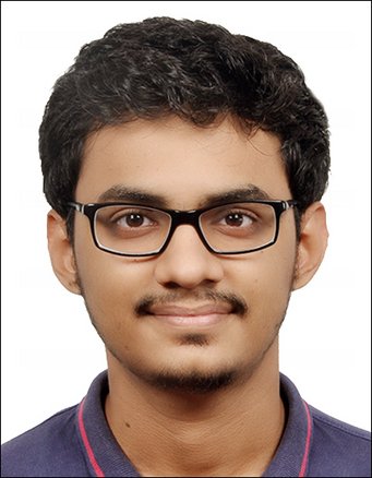 A person with short, curly black hair and prominent ears, wearing a dark polo shirt featuring red piping along the collar.