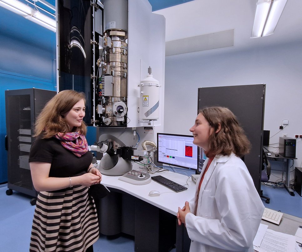 Julia Eisentraut (links), Mitglied des Landtags NRW und Sprecherin für Wissenschaft und Digitalisierung der Landtagsfraktion von BÜNDNIS 90/DIE GRÜNEN bei der Diskussion mit Raquel Aymerich Armengol, Doktorandin am Max-Planck-Institut für Eisenforschung. Zu sehen ist das Transmissionselektronenmikroskop welches Aymerich Armengol unter anderem für die Analyse von Katalysatoren zur Herstellung von grünem Wasserstoff verwendet.