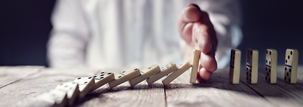 Conflict Management Hand halts falling dominoes on wooden surface.