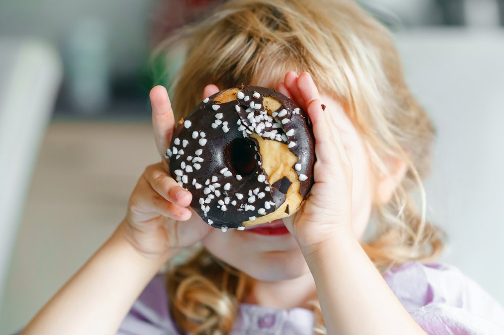 A girl holds a donut in front of her face.
