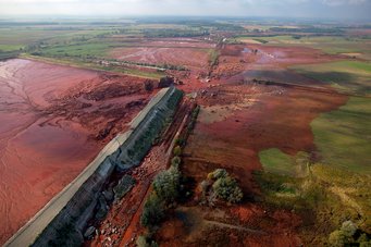 Der aggressive Rotschlamm greift auch Beton an. So brach im Oktober 2010 brach der Damm einer Rotschlamm-Deponie nahe der ungarischen Stadt Ajka. Mehr als eine Million Kubikmeter strömten daraufhin in die Umwelt und drei nahegelegne Dörfer. Solche Umweltkatastrophen ließen sich künftig vermeiden, wenn der Rotschlamm für die Stahlproduktion genutzt würde. In der linken Bildhälfte ist eine rechteckige Rotschlammdeponie zu sehen. Etwa in der Bildmitte ist zu erkennen, dass der Damm der Deponie an einer Ecke gebrochen ist, sodass die umliegende Landschaft auf einer Fläche, etwa so groß wie die Deponie selbst mit Rotschlamm geflutet wurde.