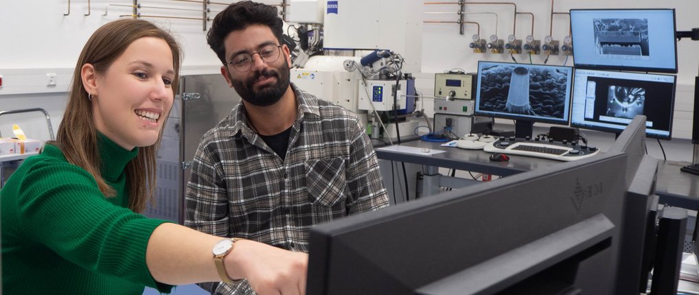 Zwei Personen betrachten Analysebilder auf mehreren Monitoren in einem Labor.