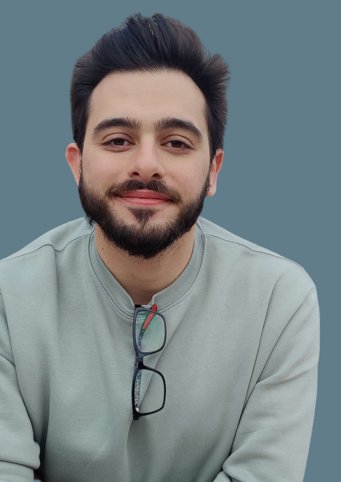 A person is dressed in a grey sweater with black-rimmed glasses hanging from the collar, set against a solid grey-blue background.
