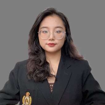 A person is dressed in a formal black blazer with a detailed emblem on the left side, featuring a crown and laurel design. The background is a neutral grey, providing a professional and unobtrusive setting. The attire suggests a formal or official context.