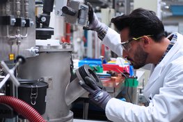 Person in a lab coat and with protective glasses looking into the analytic chamber of an electric arc furnace.