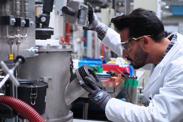 Person in a lab coat and with protective glasses looking into the analytic chamber of an electric arc furnace.