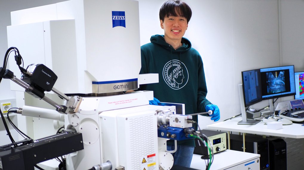 A researcher in a green hoodie with the Max Planck logo stands beside advanced laboratory equipment.