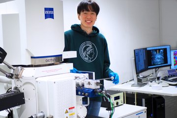 A researcher in a green hoodie with the Max Planck logo stands beside advanced laboratory equipment.