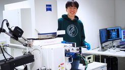 Wissenschaftler bedient ein Elektronenmikroskop; im Hintergrund sind Computerbildschirme sichtbar.