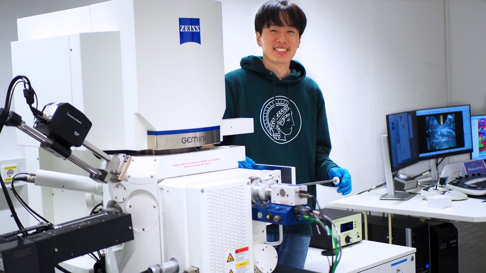 Wissenschaftler bedient ein Elektronenmikroskop; im Hintergrund sind Computerbildschirme sichtbar.