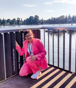 Person in rosa Anzug kniet auf Pier bei sonnigem Wetter.