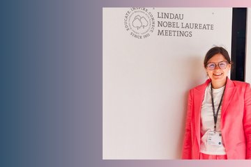 Person in pink suit in front of beige wall with logo.