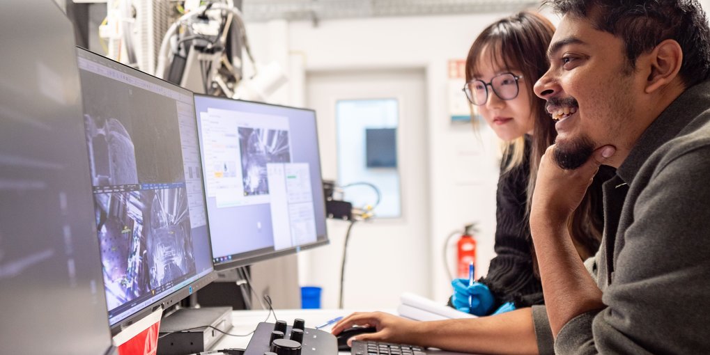 Two persons looking at screens showing images from a microscope