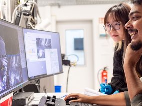 Two persons looking at screens showing images from a microscope