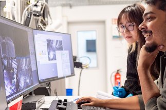 Two persons looking at screens showing images from a microscope
