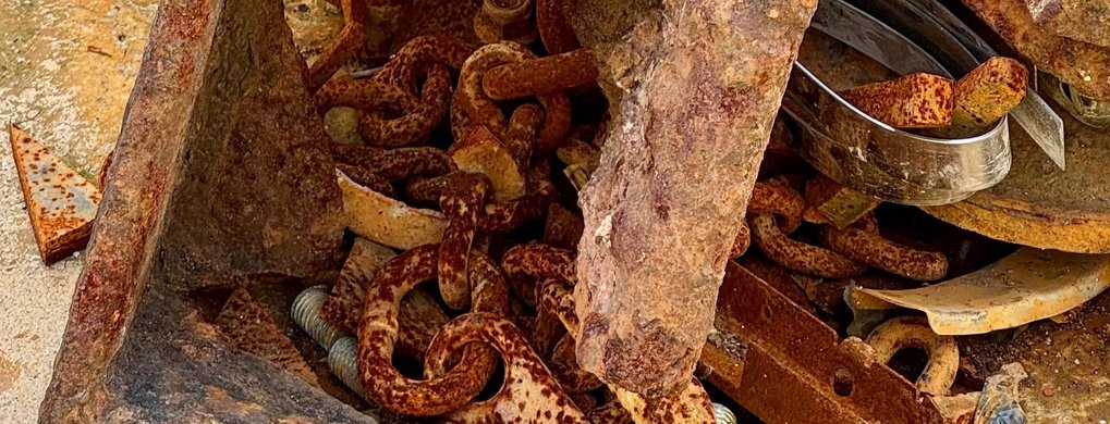 A pile of rusted metal chains, bolts, and plates resting on a weathered concrete surface.