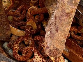 A pile of rusted metal chains, bolts, and plates resting on a weathered concrete surface.