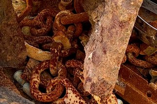 A pile of rusted metal chains, bolts, and plates resting on a weathered concrete surface.