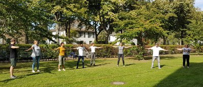 Acht Menschen stehen in einem Park in einem Halbkreis und strecken ihre Arme aus.