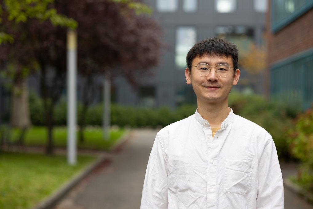 Die Deutsche Gesellschaft für Materialkunde (DGM) hat Dr. Liuliu Han mit dem DGM-Nachwuchspreis ausgezeichnet. Han ist Projektgruppenleiter am Max-Planck-Institut für Nachhaltige Materialien und forscht zu Magneten, die ohne Seltene Erden auskommen. Person in weißem Hemd steht draußen vor einem Gebäude. Im Hintergrund sind Bäume zu sehen.