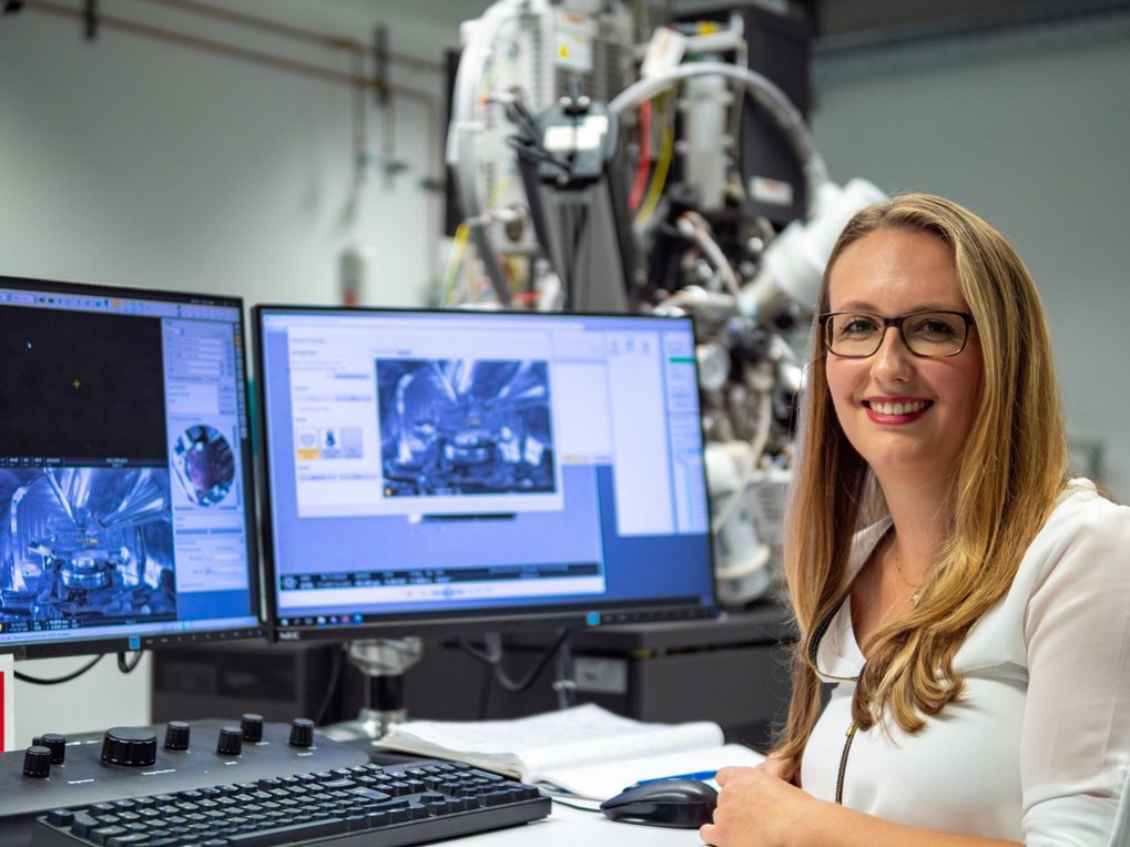 Person mit Brille sitzt vor Monitoren in einem Labor.