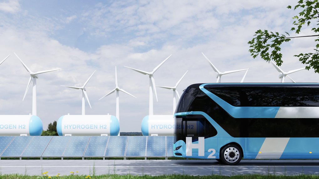 Hydrogen bus near wind turbines, solar panels and hydrogen storage tanks.