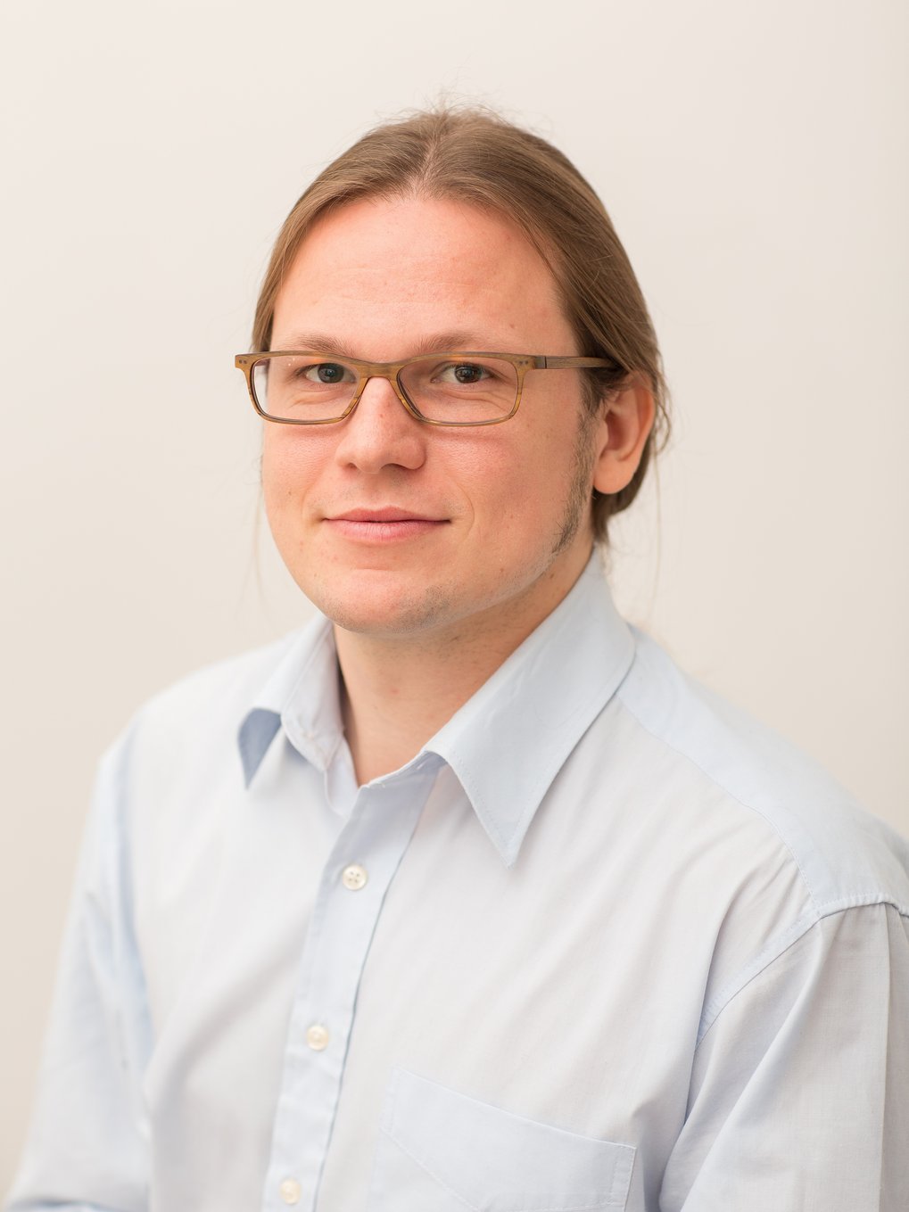 Portrait of a man with blond hair, glasses and a blue button shirt.