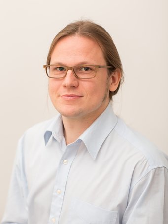 Portrait of a man with blond hair, glasses and a blue button shirt.