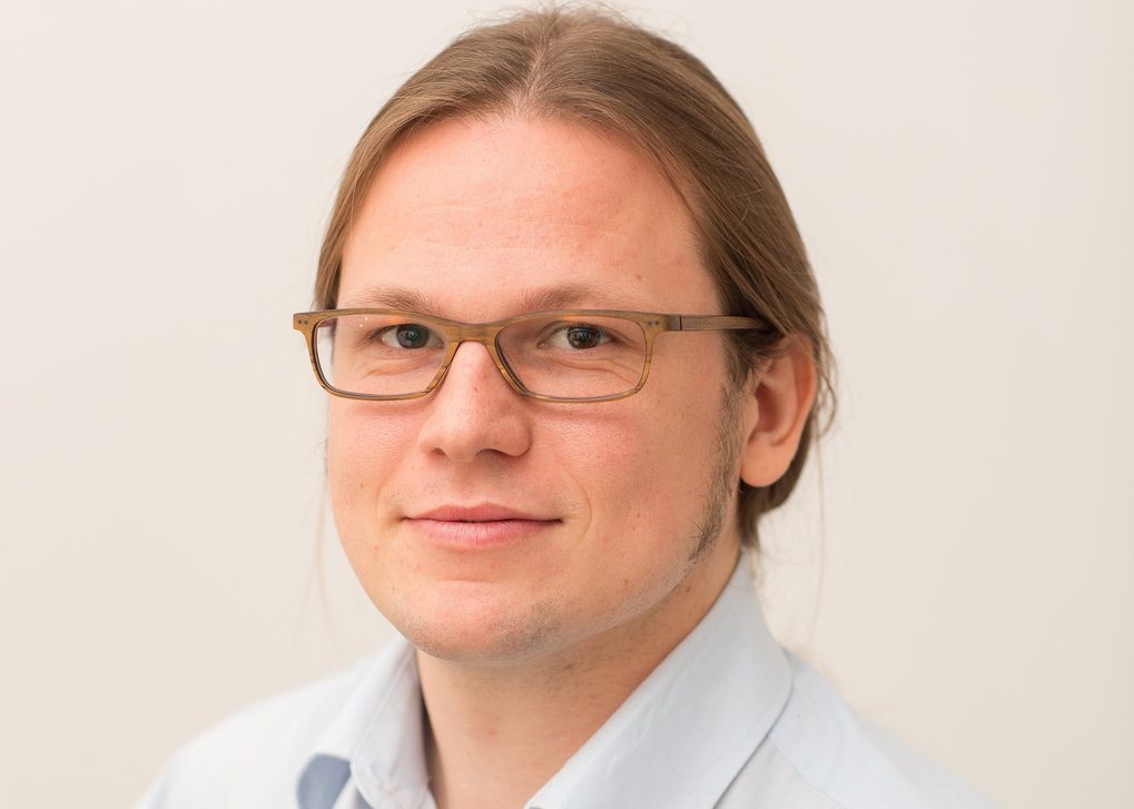 Portrait of a man with blonde hair, glasses and a blue button shirt.
