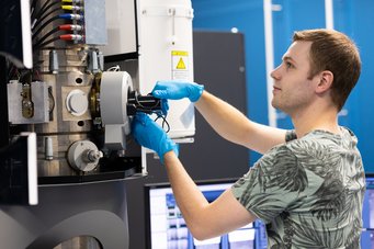 Dominique Mattlat, PhD researcher at MPI-SusMat and co-author of the publication, used scanning transmission electron microscopy to identify the zinc-oxide barriers, proving their successful deposition to block the zinc ion migration and thus prevent the decomposition of earth-abundant thermoelectric materials. Man wearing blue gloves operating a high-tech laboratory device with multiple cables and control panels.