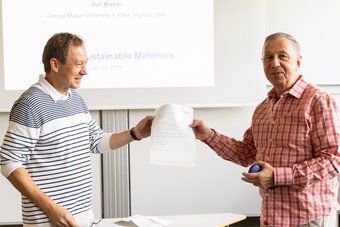 Prof. Gerhard Dehm (left) presents the Humboldt Research Award certificate to Dr Yuri Mishin. His research stay at the Max Planck Institute for Sustainable Materials marks the beginning of their collaboration under the Humboldt Research Award programme. A man hands over a certificate to another man. Both are standing in a seminar room.