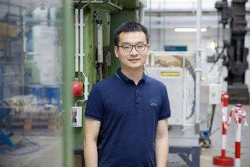 Man stands in an industrial hall. In the background is a forging hammer.