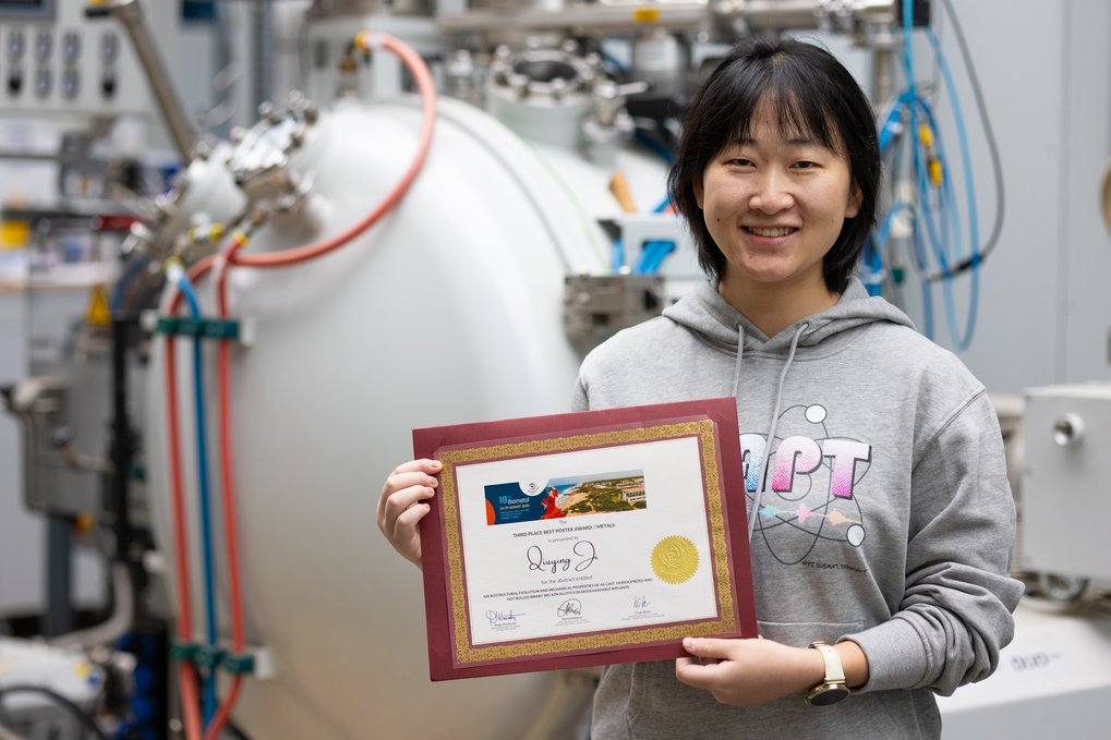 Woman holding a certificate in her hands and standing in front of industrial device.